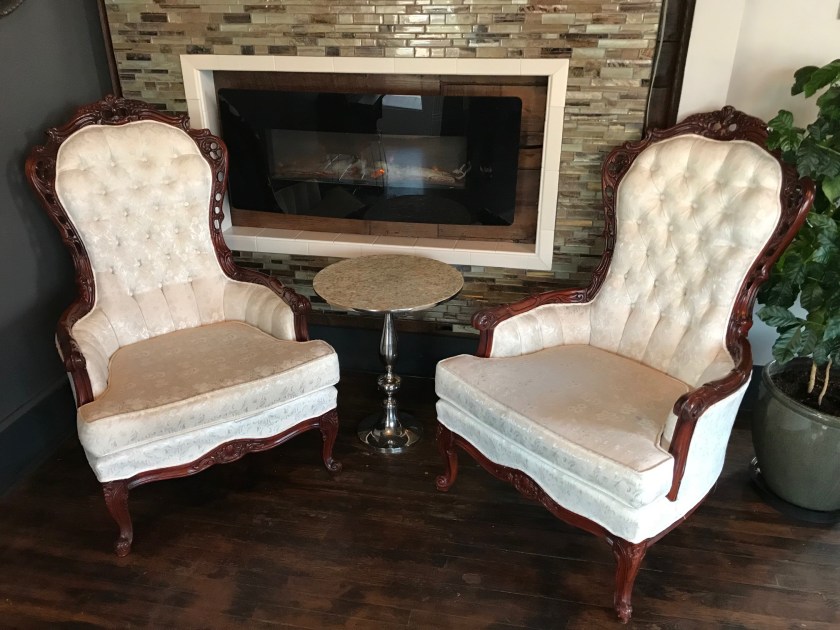 the white fabric and Wood trim on the wingback chairs near the front entrance perfectly complement the Victorian aesthetic
